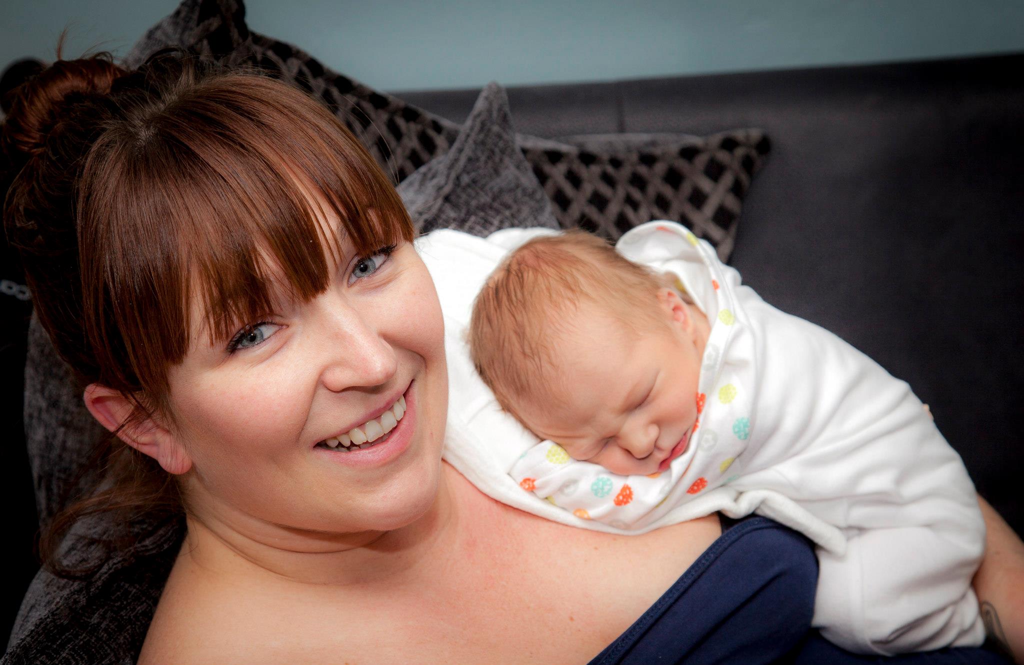 Gorgeous mum with her tiny newborn son, smiling at the camera
