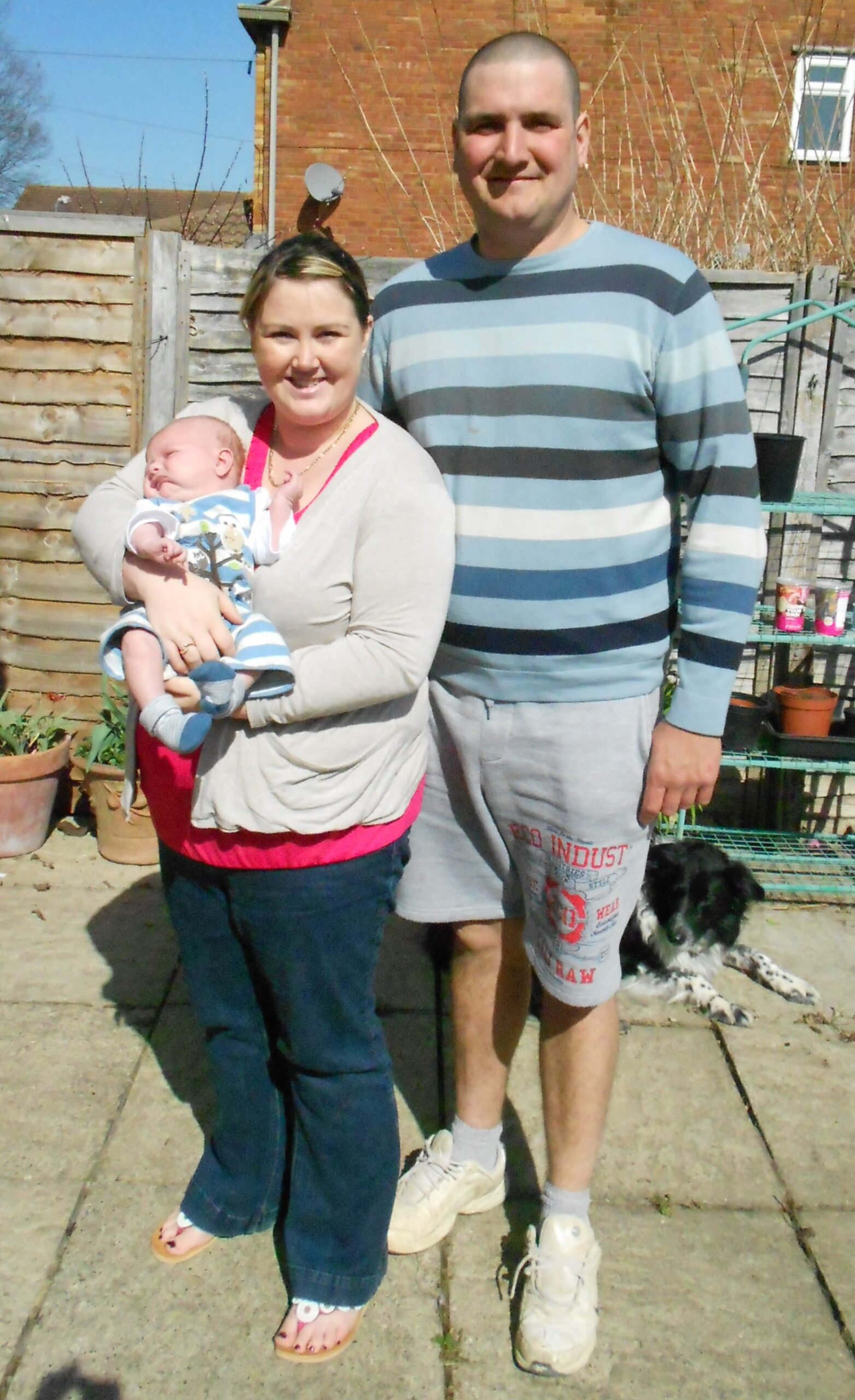 Mum, dad holding their new baby in the garden on a sunny day