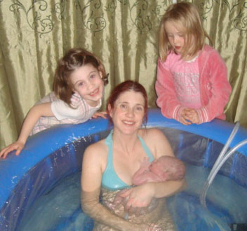 Mum and newborn in the birthing pool surrounded by big sisters E and F. All smiling broadly